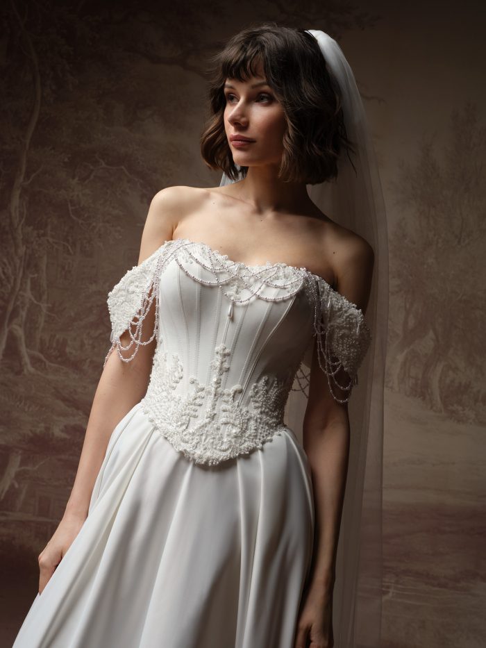 Close-up of the Corazon veil from Maggie Sottero's Essentials Edit collection, showing the sheer tulle draped beside an off-the-shoulder beaded corset bodice with draped pearl trim.