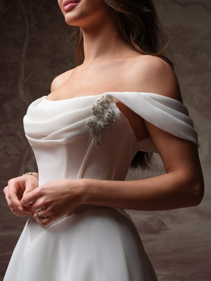 Close-up detail of the Maggie Sottero Abilene A-line wedding gown featuring an off-the-shoulder draped neckline, embellished accents, and a structured satin bodice.