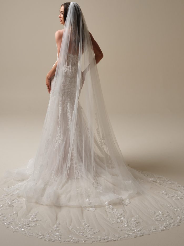 Back view of the Benjie fit-and-flare wedding dress by Maggie Sottero, featuring a strapless lace-appliquéd bodice with button back detail and a cathedral veil with beaded floral edge trim.
