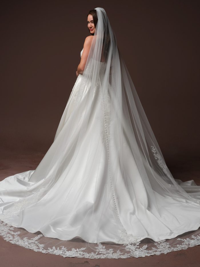 Back view of the Landis wedding dress by Maggie Sottero, showing the button-back bodice and satin ball gown train with a lace-trimmed cathedral veil.