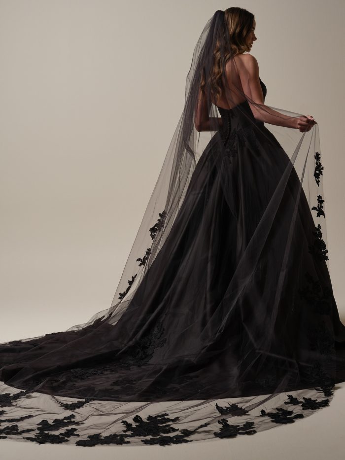 Back view of the Serafina black ball gown wedding dress by Maggie Sottero, showing the corset back detail and full satin ball gown skirt with a flowing floral lace-trimmed veil.