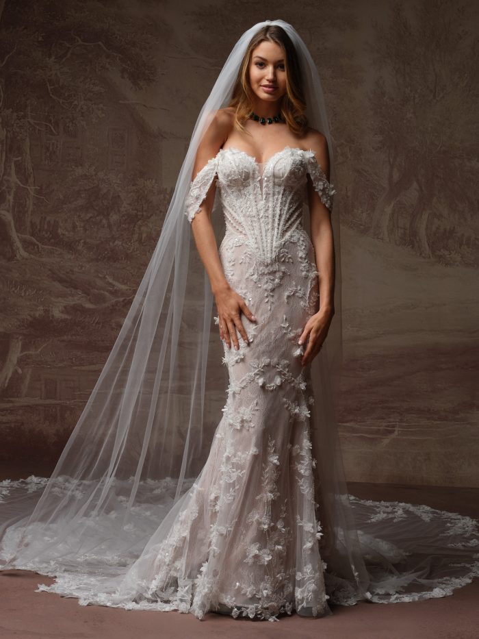Bride wearing the Stasia wedding dress by Maggie Sottero, featuring an off-the-shoulder corset bodice with 3D floral lace appliqué and a fitted mermaid skirt, paired with a cathedral veil.
