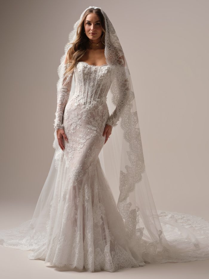 Bride wearing the Takera veil by Maggie Sottero, a mantilla-style veil with all-over floral lace, paired with a long-sleeve lace mermaid wedding gown.