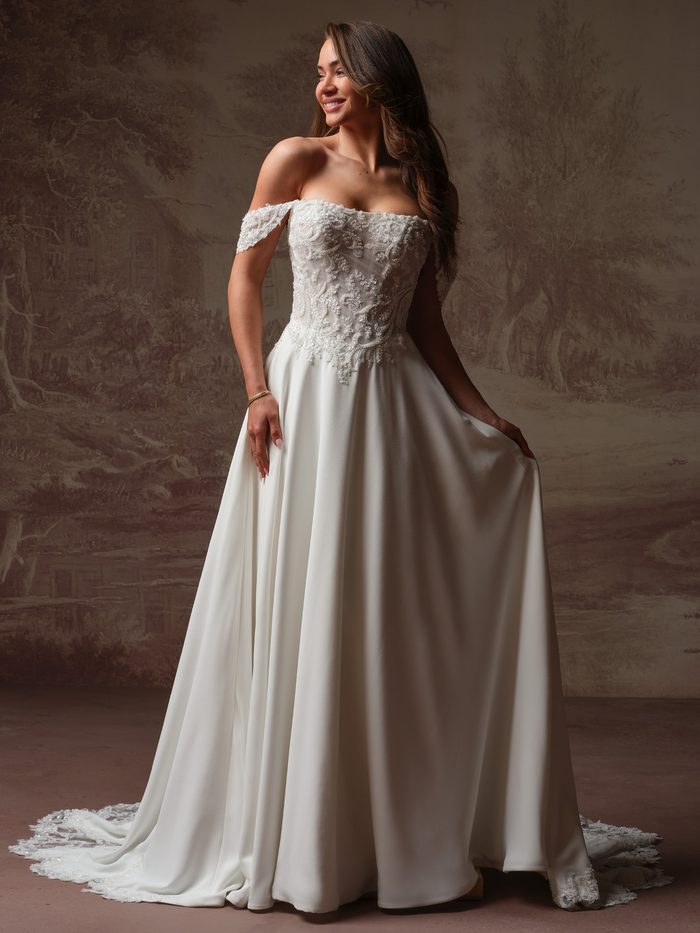 Rebecca Ingram Hazel A-line wedding gown featuring an off-the-shoulder lace bodice, satin skirt, and a flattering silhouette for petite brides.