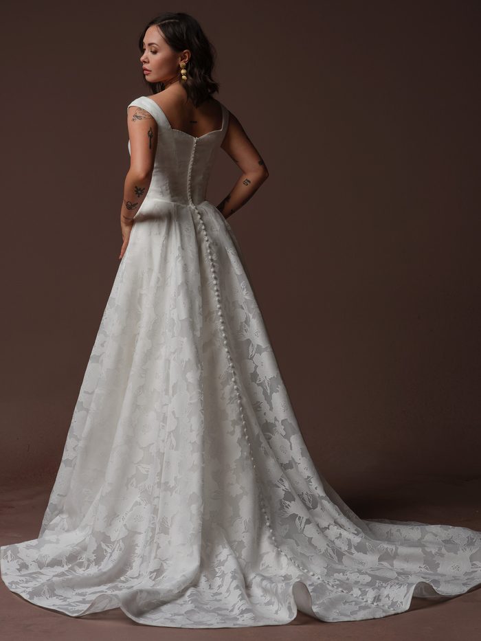 Back view of the Rebecca Ingram Jade A-line wedding gown featuring covered buttons, floral jacquard, and a flowing train.