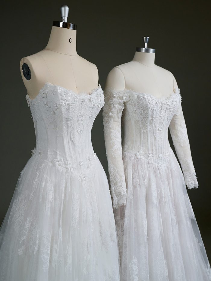 Close-up view of two Kitaro by Maggie Sottero wedding gowns displayed on dress forms. Both feature a lace-covered corset bodice with floral appliqués, delicate beadwork, and a sweetheart neckline. The left gown showcases the strapless design, while the right gown is styled with detachable off-the-shoulder long sleeves made from matching lace, highlighting the gown’s customizable sleeve option.