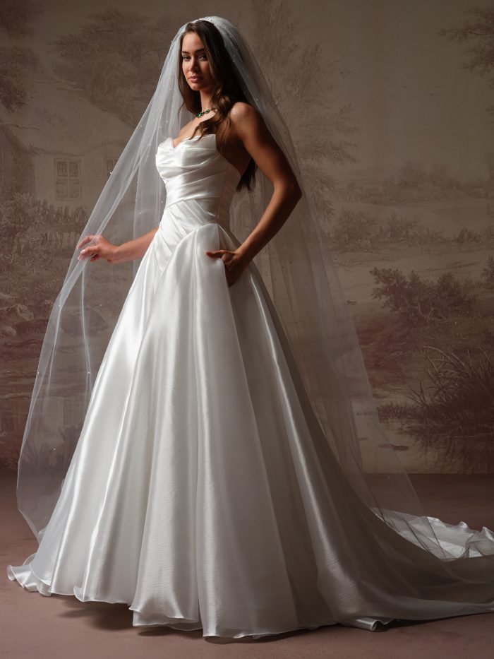 Essentials Edit Wedding Dress Veil, full-length cathedral veil scattered with delicate pearls, styled with a strapless satin ballgown featuring a draped sweetheart bodice and full pleated skirt with pockets.