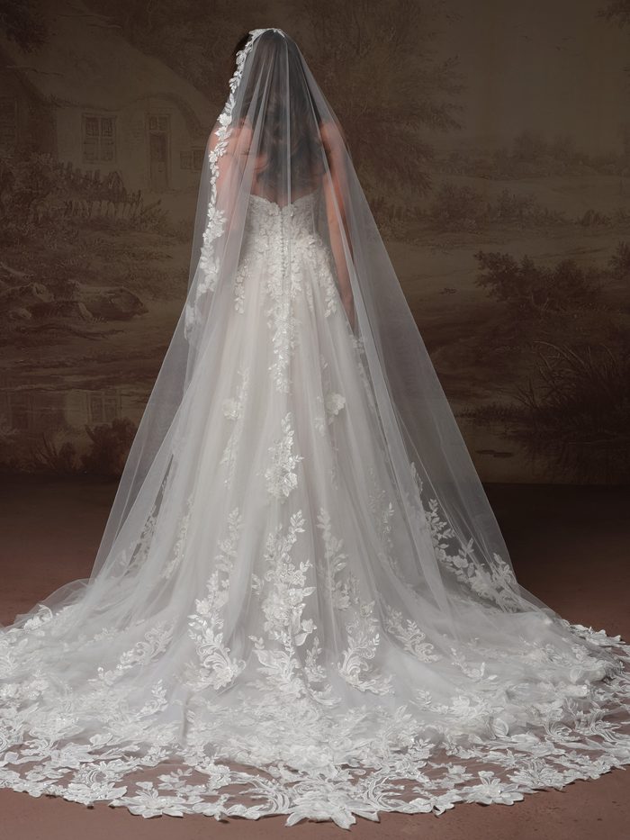 Back view of the Bellevue Cape accessory by Maggie Sottero, featuring a dramatic cathedral-length cape crafted from delicate floral lace. The cape includes an attached lace hood and cascades from the shoulders into a sweeping train, showcasing intricate lace motifs and scalloped edges throughout the design.