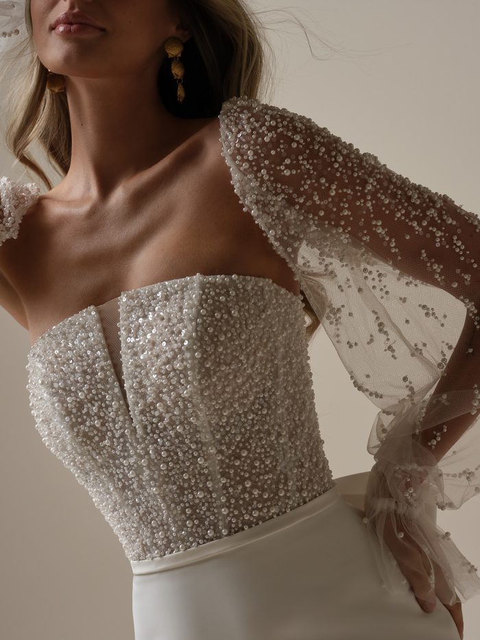 Rebecca Ingram Heyda Sheath Wedding Dress, close-up detail of the densely pearl and sequin-covered strapless corset bodice with sheer bishop sleeves scattered in pearls and finished with a ruffled tulle cuff.