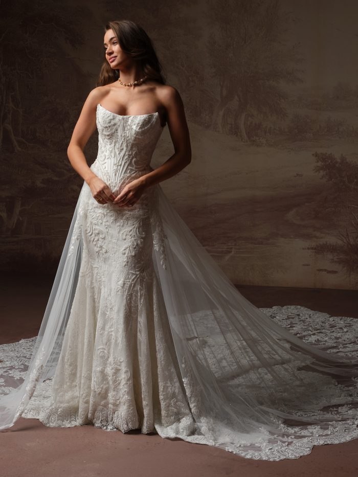 Sottero and Midgley Eirawen, full-length front view of the strapless fit-and-flare lace wedding gown with a structured corset bodice, allover floral lace skirt, and a dramatic detachable cathedral-length tulle train with lace-trimmed edging.