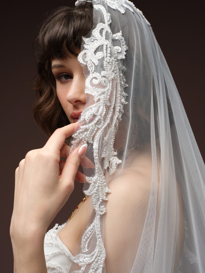 Close-up of a Maggie Sottero bridal veil with intricate lace edging and pearl beading, styled over a strapless gown.