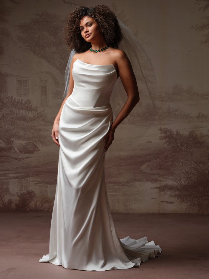 Astoria by Maggie Sottero from the Essentials Edit, showcasing a minimalist satin sheath wedding gown with a draped neckline and long, flowing train, styled with a soft tulle veil.