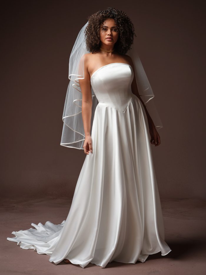 Bali by Maggie Sottero from the Essentials Edit, showcasing a minimalist strapless satin A-line wedding gown with a clean bodice and flowing skirt, styled with a soft tulle fingertip veil.