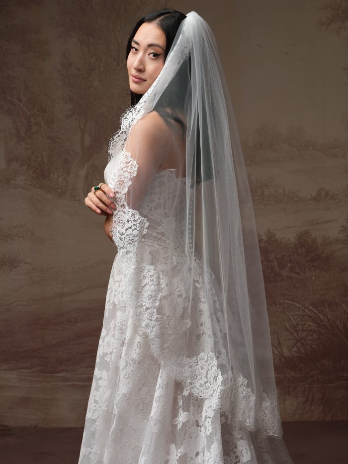 Minuet by Maggie Sottero veil from the Essentials Edit, featuring a fingertip-length tulle veil with delicate lace trim along the edge, styled over a lace wedding gown in a close-up side view.