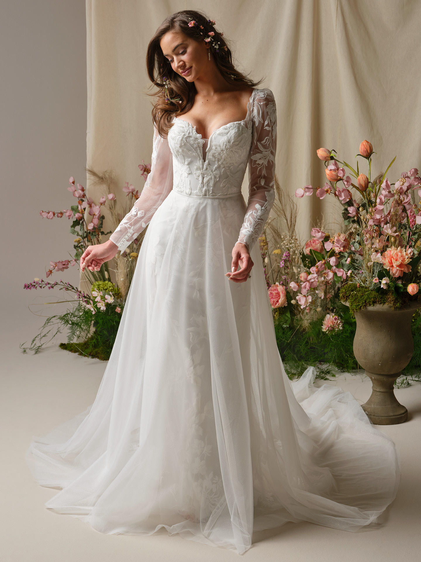 Bride wearing a sparkle tulle overskirt from the Maggie Sottero Essentials Edit, featuring soft shimmering layers that add airy volume and a flowing train over a long-sleeve lace A-line wedding gown.