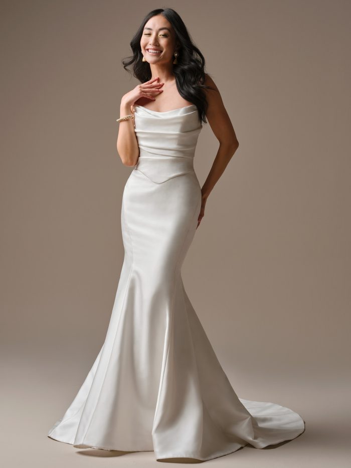 Full-length view of the Maureen Lane fit-and-flare wedding dress by Maggie Sottero featuring a sleek satin silhouette, asymmetrical ruched bodice, and dramatic cat-eye neckline.