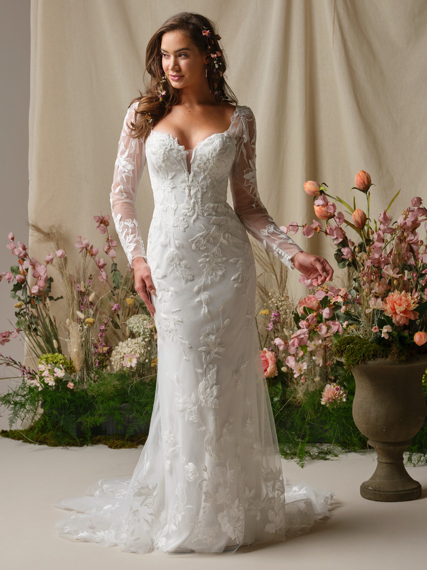 Bride wearing Aubra by Rebecca Ingram, a long-sleeve lace sheath wedding dress featuring an illusion sweetheart neckline, fitted silhouette with floral lace appliqués, and a soft lace train.