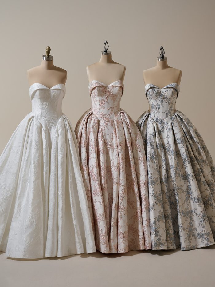 Three Sottero and Midgley Aberdeen ballgown wedding dresses displayed on mannequins in ivory, blush, and blue floral jacquard, each featuring a strapless sweetheart neckline, corset bodice, and voluminous pleated skirt.
