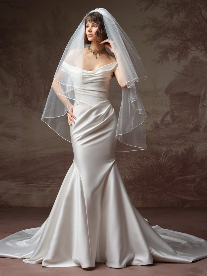 Front view of the Amor by Maggie Sottero fingertip wedding veil from the Essentials Edit collection, a two-tier plain-edge tulle veil, styled over a strapless off-the-shoulder satin mermaid gown with a cathedral train.