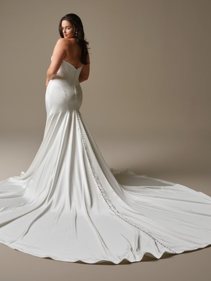 Back view of Maggie Sottero Sinclaire fit-and-flare wedding dress with a strapless corset, covered button detailing, and a dramatic flared train, highlighting a sleek, curve-enhancing silhouette.