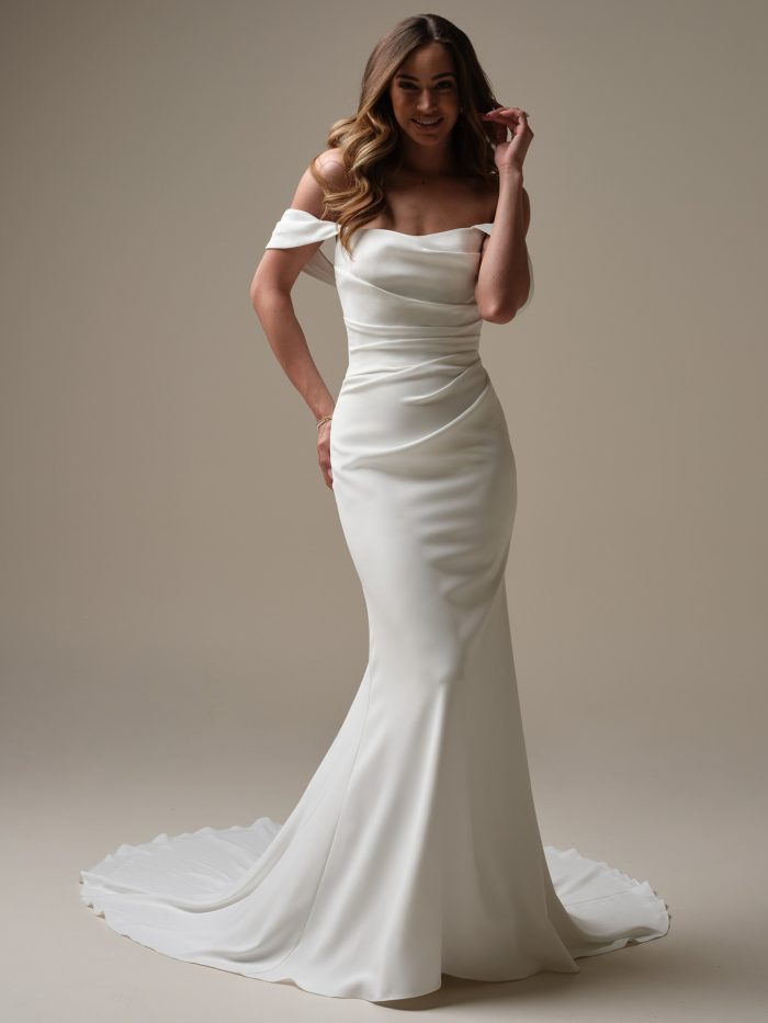 Denise sheath wedding dress by Rebecca Ingram featuring an off-the-shoulder neckline, draped bodice, and fitted silhouette.