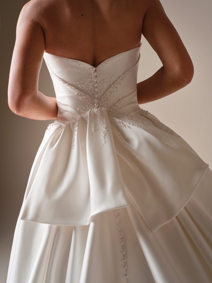 Strapless satin ball gown wedding dress with oversized bow, button-back detail, and train.