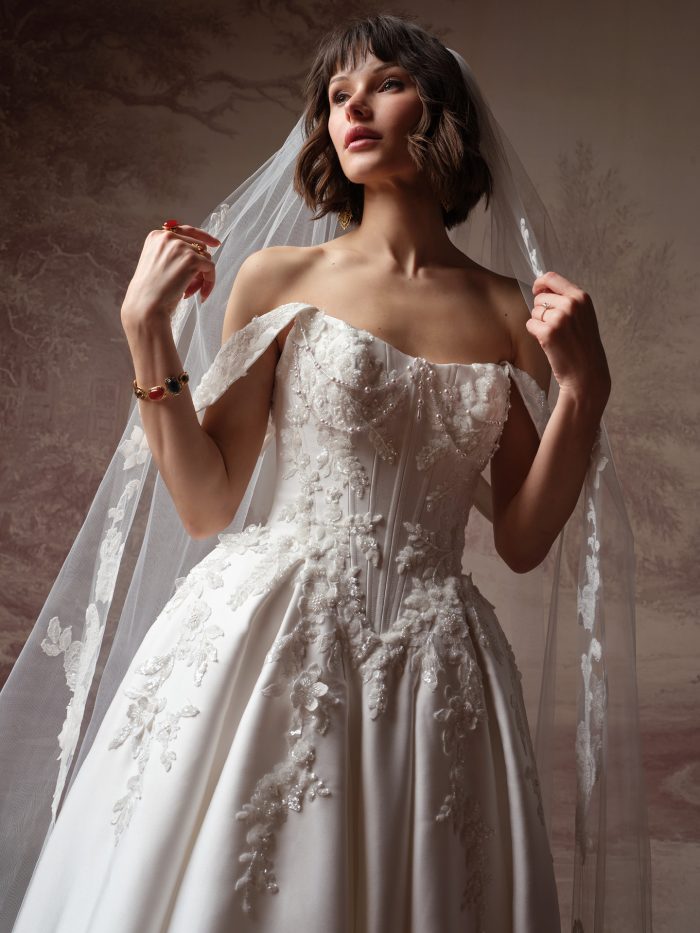 Sottero and Midgley Petra ballgown wedding dress, close-up detail — beaded floral lace bodice with off-the-shoulder straps and satin ballgown skirt, shown with lace-edged veil.