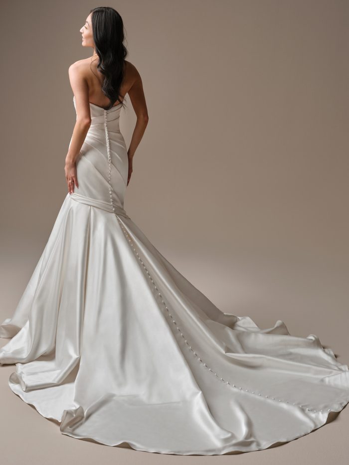 Maggie Sottero Emelina fit-and-flare wedding dress back view with asymmetric draped bodice and cathedral train with covered buttons