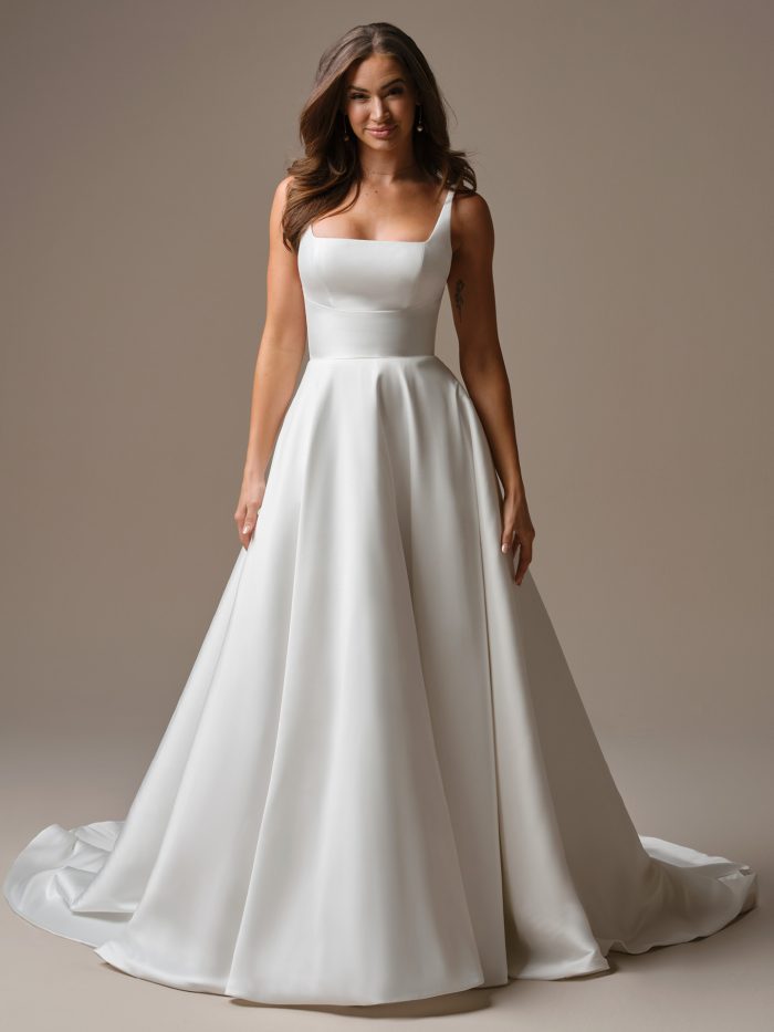 Full-length front view of Galina by Maggie Sottero an A-line wedding dress featuring a clean, structured bodice with a square neckline and wide straps, paired with a smooth, full skirt that flows into a soft train, photographed against a neutral studio background.