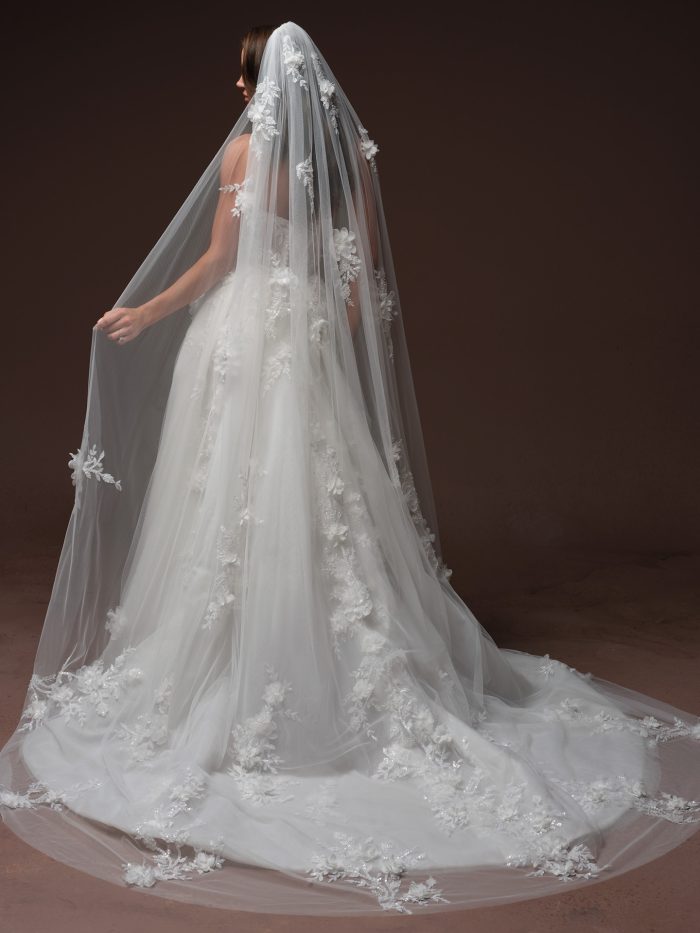 Back view of the Maggie Sottero Fern wedding dress paired with the coordinating Fern cathedral veil, both adorned with matching 3D floral and embroidered lace appliqués. The veil extends into a dramatic train that pools on the floor, with floral appliqués scattered across the tulle and densely placed along the scalloped edge.