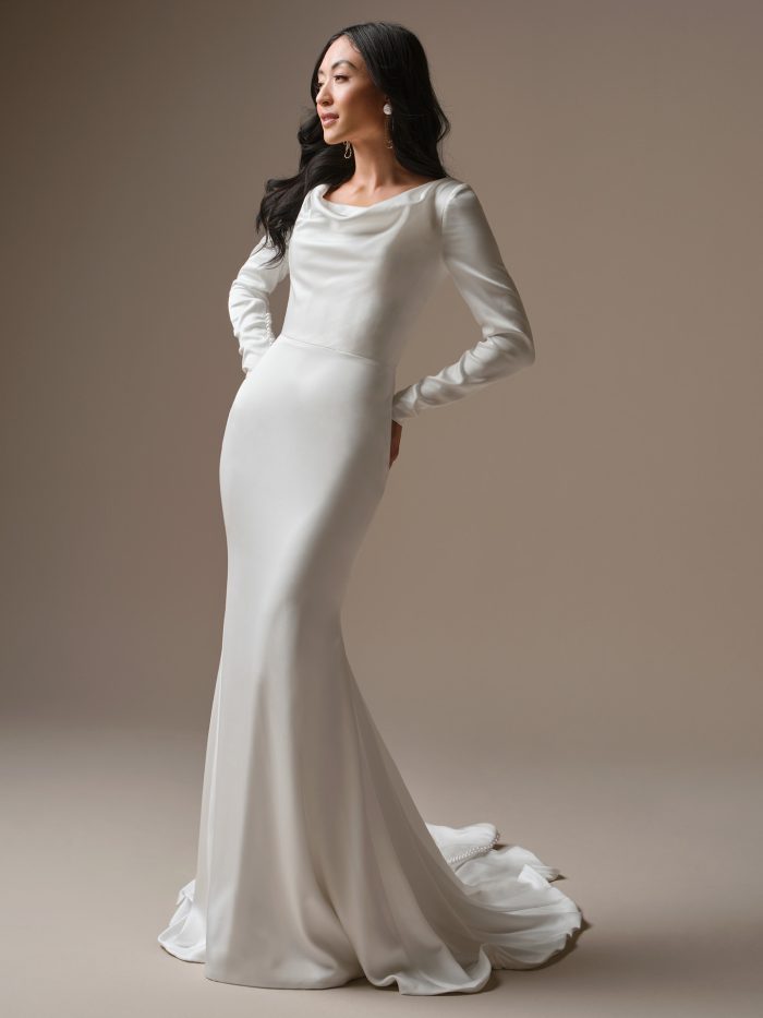 Maggie Sottero Melinda sheath wedding dress in sleek satin with a draped cowl neckline, fitted long sleeves with pearl button cuffs, and a flowing chapel train with a ruffled lace hem.