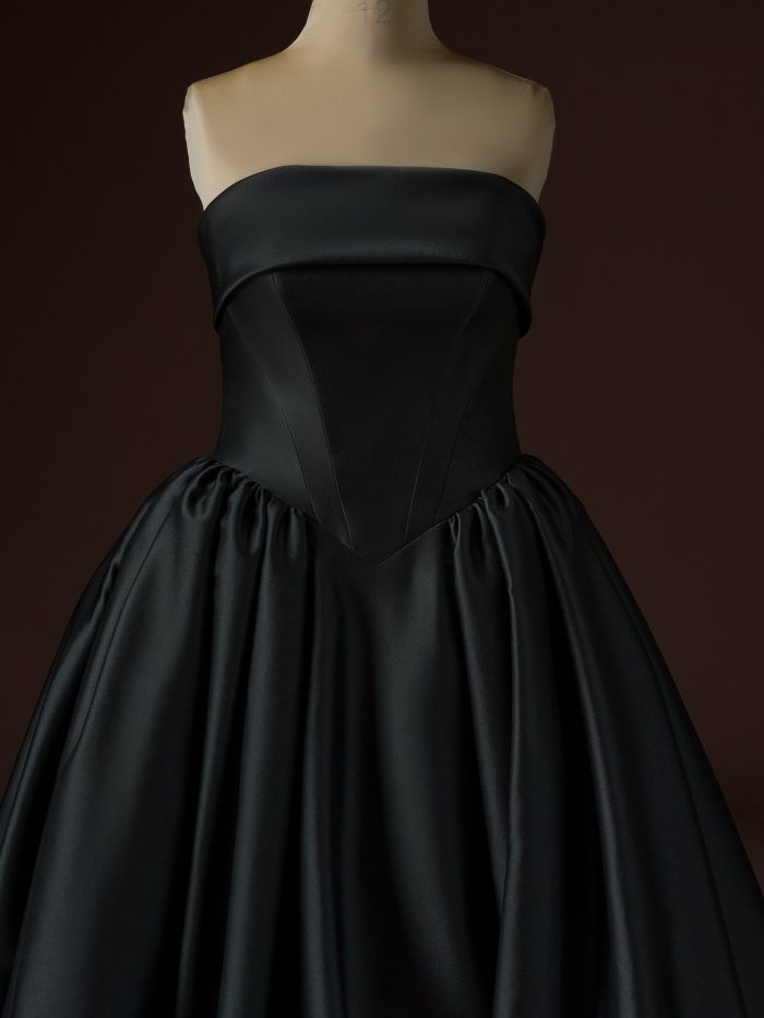 Rane ballgown wedding dress by Maggie Sottero in black, shown in a close-up view highlighting the strapless folded neckline, sculpted corset bodice with contoured seams, and the beginning of the full, softly gathered skirt in smooth satin.