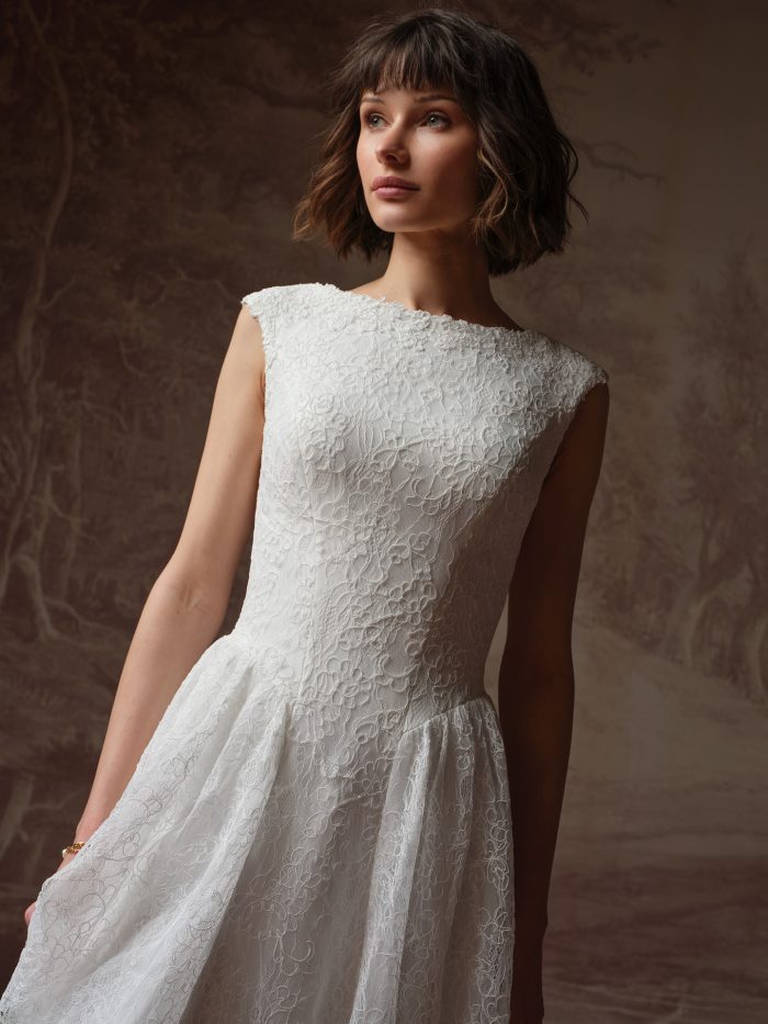 Briar A-line wedding dress by Rebecca Ingram in a close-up view highlighting the bateau neckline, cap sleeves, and intricate lace texture across the bodice and upper skirt.