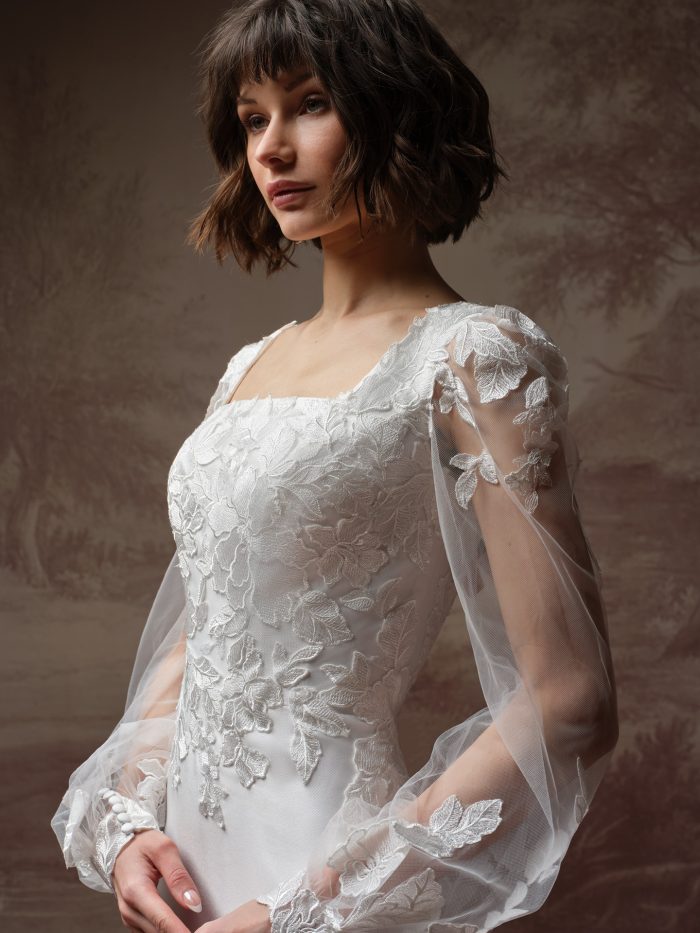 Goldie Leigh fit-and-flare wedding dress by Rebecca Ingram in a close-up view highlighting the square neckline, dimensional floral lace appliqués, and sheer illusion sleeves with delicate detailing.