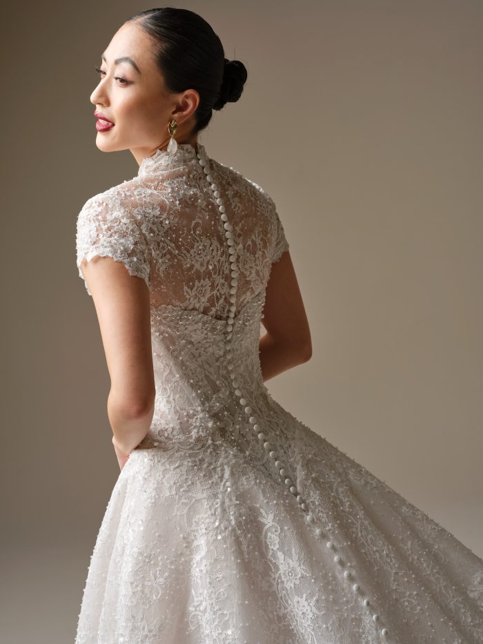 Angelica A-line wedding dress by Sottero and Midgley in a close-up back view highlighting the illusion lace detailing, cap sleeves, and a row of covered buttons running down the sheer back over the fitted bodice.