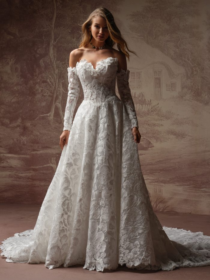 Sottero and Midgley Merrigan A-line wedding dress in heavily embellished floral lace with a sweetheart neckline edged in 3D ruffled flower petals, detachable sheer long sleeves with matching petal trim at the shoulder and pearl button cuffs, and a full cathedral train.