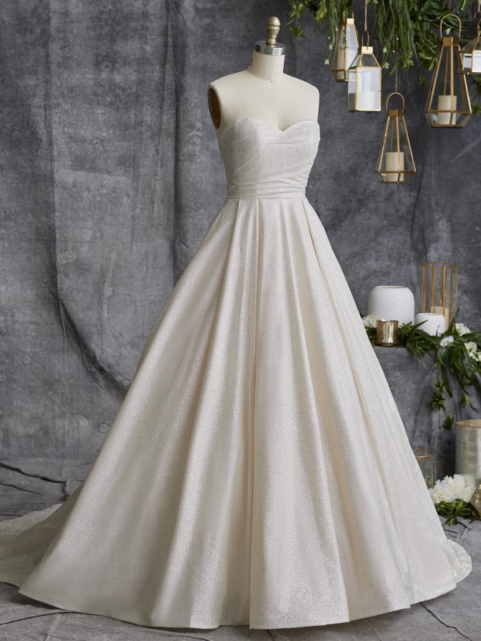 Front view of the Anniston ball gown wedding dress by Maggie Sottero on a dress form, featuring a strapless sweetheart neckline with ruched bodice and a full shimmer tulle ball gown skirt with train.