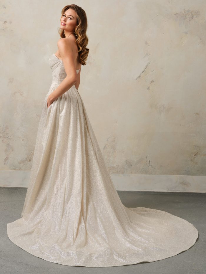 Side/back view of the Anniston Lane wedding dress by Maggie Sottero, showing the strapless sweetheart bodice with fitted shimmer skirt and flowing detachable overskirt train.