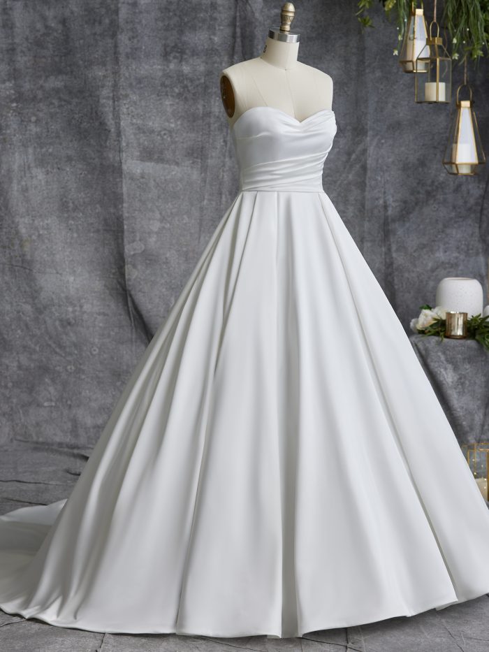 Front view of the Anniston Marie ball gown wedding dress by Maggie Sottero on a dress form, featuring a strapless sweetheart neckline with ruched bodice and a full satin ball gown skirt with train.