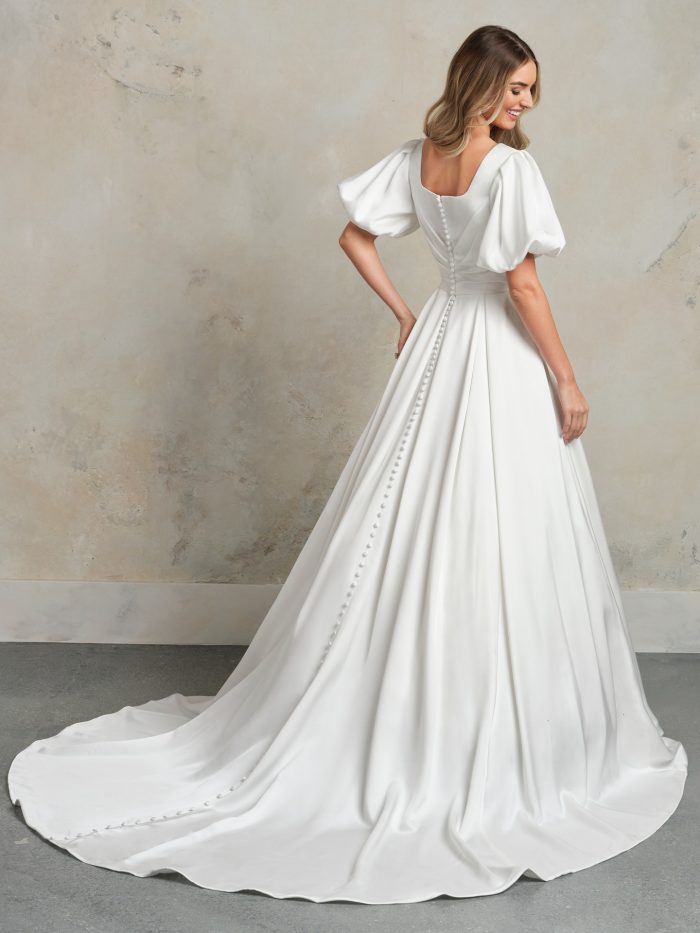 Back view of the Anniston Marie Leigh ball gown wedding dress by Maggie Sottero, showing a modest square back with puffed short sleeves and covered button closure down the full satin ball gown skirt and train.