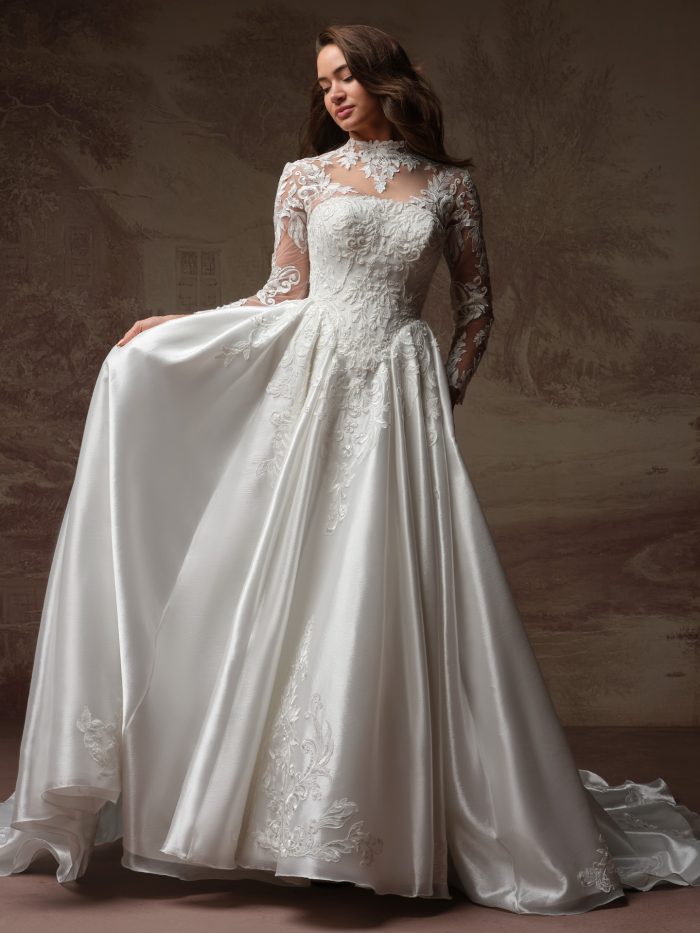 Bride wearing the Dahlia ballgown wedding dress, featuring a high illusion lace neckline, sheer long lace sleeves, an embroidered lace bodice, and a voluminous satin ballgown skirt with lace appliqué at the hem.