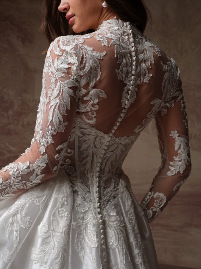 Back view of the Dahlia gown by Maggie Sottero, showing the sheer lace back with a row of covered buttons and detailed floral lace sleeves.