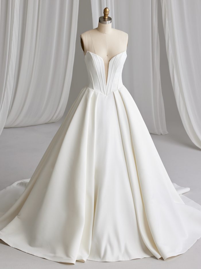 Front view of the Derrick ball gown wedding dress by Maggie Sottero on a dress form, featuring a deep plunging strapless neckline with structured seaming and a full satin ball gown skirt with train.