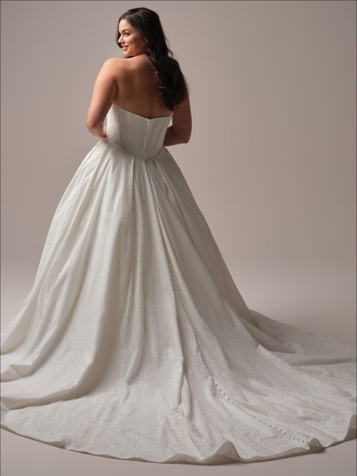Back view of the Derrick Royale ball gown wedding dress by Maggie Sottero in curve fit, showing a low sweetheart back with covered button closure down the full shimmer ball gown skirt and scalloped train.