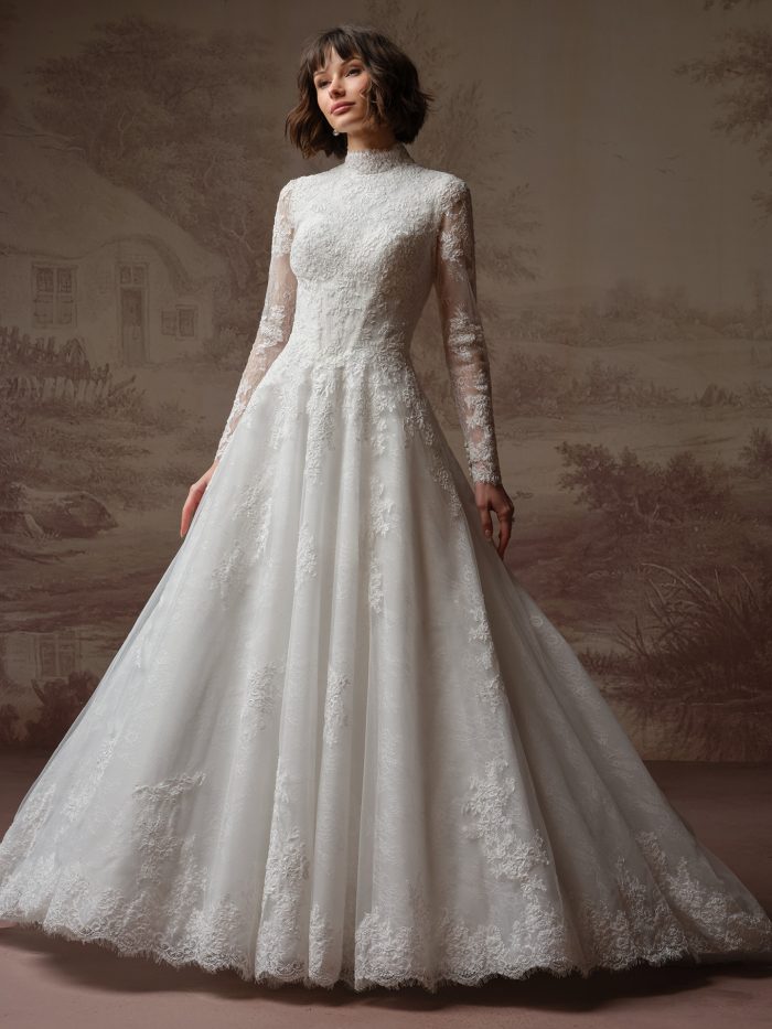 Bride wearing the Dominique ballgown wedding dress, featuring a high lace neckline, sheer long lace sleeves, an embroidered lace bodice, and a full lace ballgown skirt with a scalloped hem.