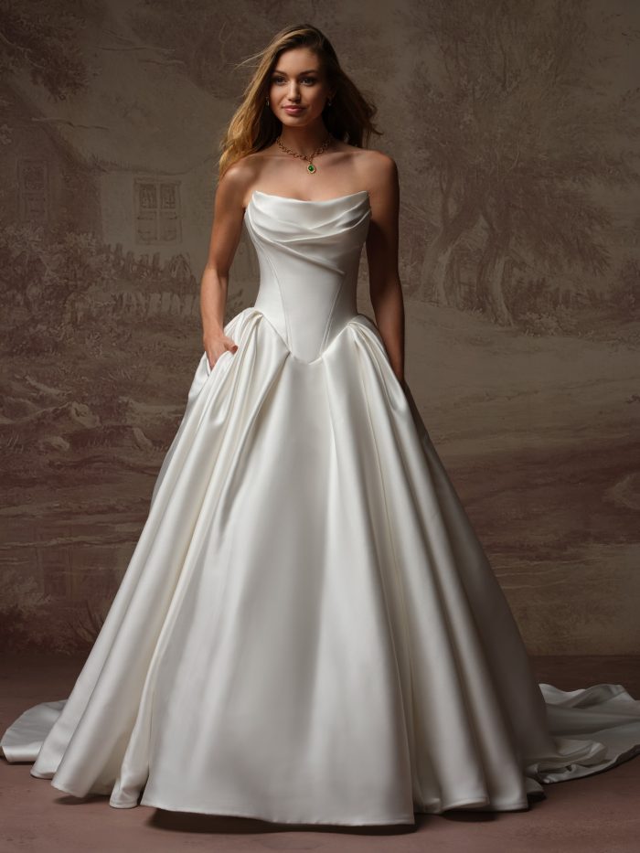 Bride wearing the Fiorita ballgown wedding dress, featuring a draped strapless satin bodice with a cowl neckline and a smooth satin ballgown skirt with side pockets and a sweeping train.