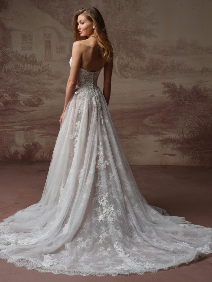 Maggie Sottero Hadley A-Line wedding dress in ivory, back view showing open low back with covered button closure, flowing tulle skirt with cascading floral lace appliqués, and cathedral train with scalloped lace border.