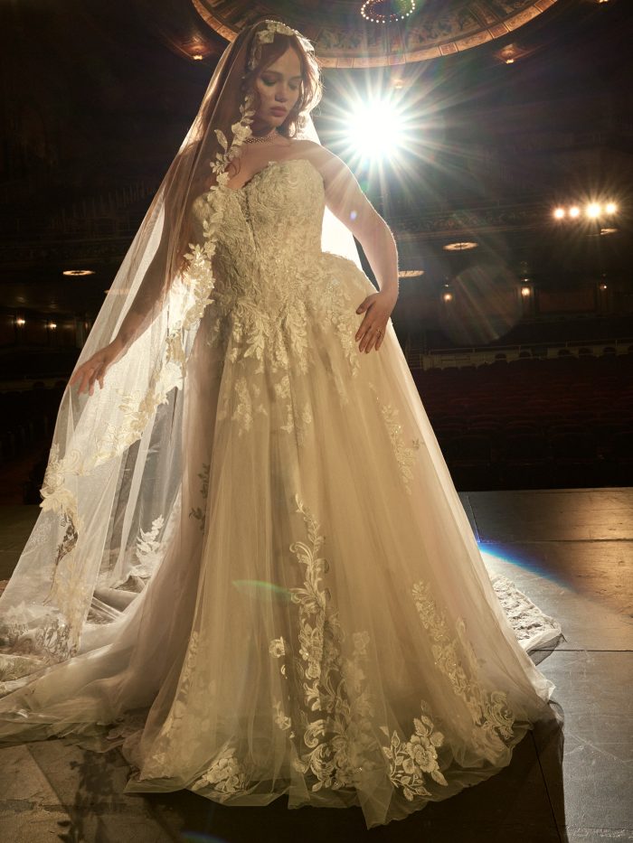 Maggie Sottero Kate A-line wedding dress in ivory, curve fit — strapless sweetheart neckline with floral lace and beaded appliqués over a full tulle ballgown skirt, styled with a long cathedral veil in a theater setting.