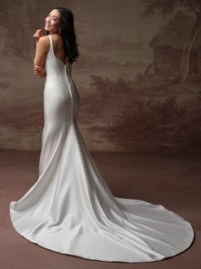 Back view of the Melissa Marie wedding dress by Maggie Sottero, showing a low scoop back with covered button closures running down the fitted satin skirt and train.