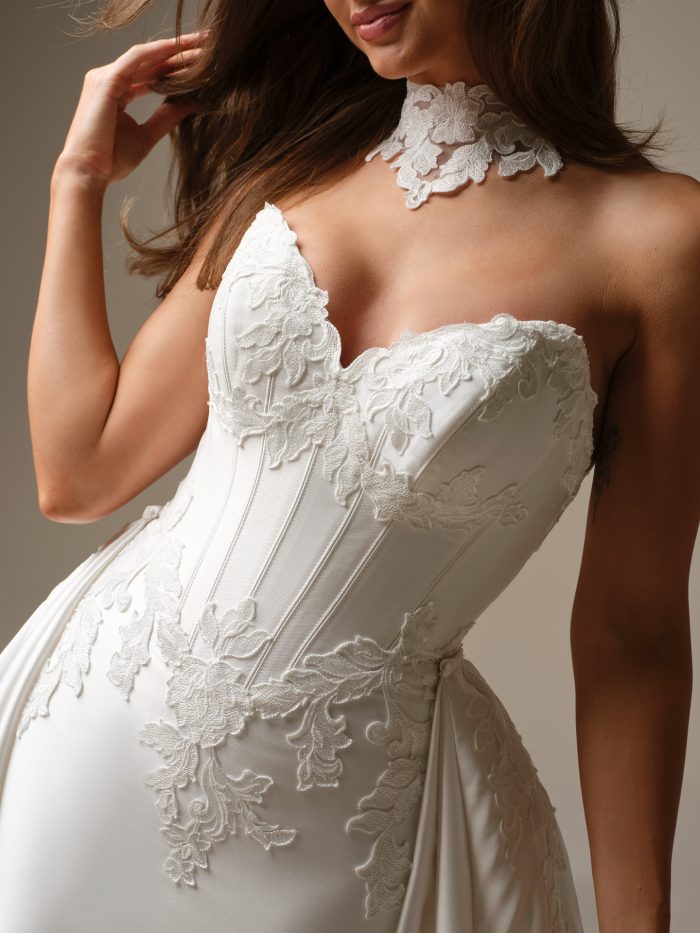Close-up of a bride wearing the Serafina Lane gown by Maggie Sottero, showing a floral lace corset bodice with a scalloped sweetheart neckline and a detachable lace choker.